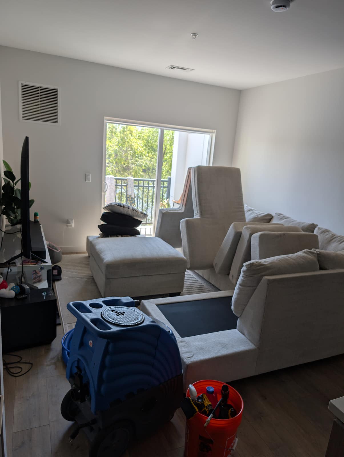 Cream sectional in a modern NJ apartment with balcony doors, blue portable extractor and bucket mid-job